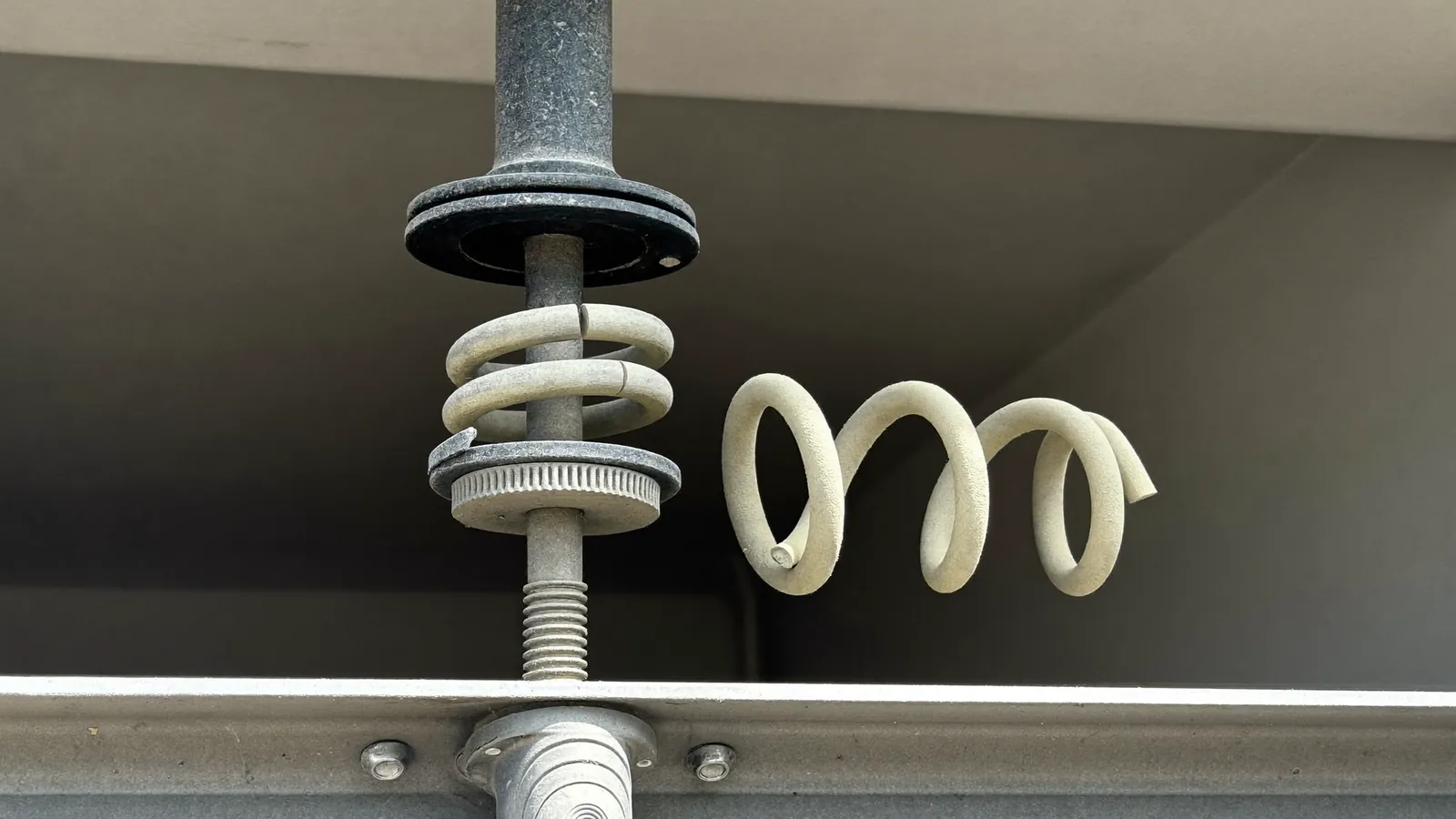 Close-up of a snapped torsion spring on the shaft above a garage door, a two-inch gap between the broken coils, fine dust on the shaft and bearing plate