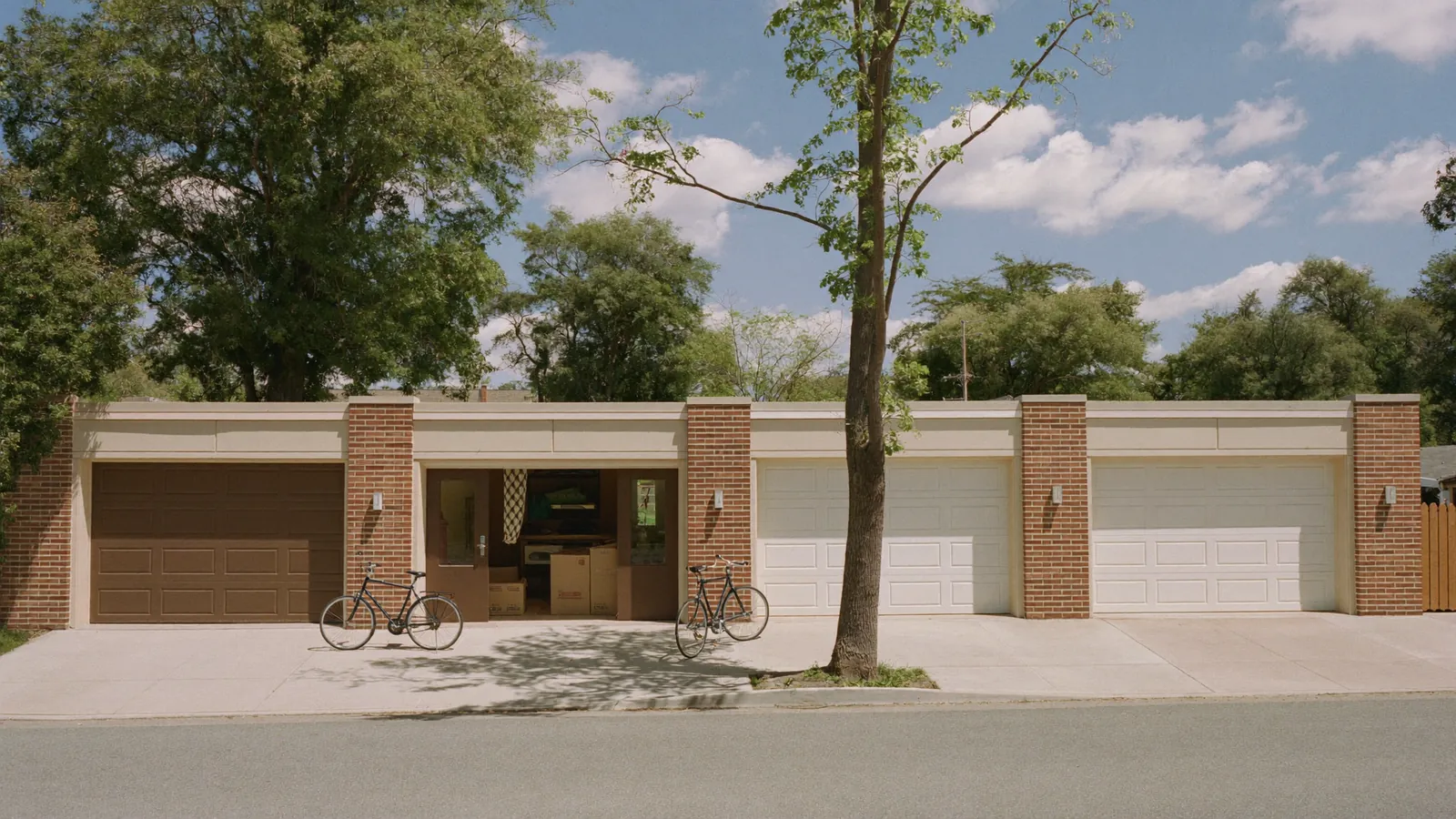 Row of single-car garage doors on a brick duplex rental near Texas Tech in Lubbock, Texas, one door open with moving boxes inside, student bicycles by the curb