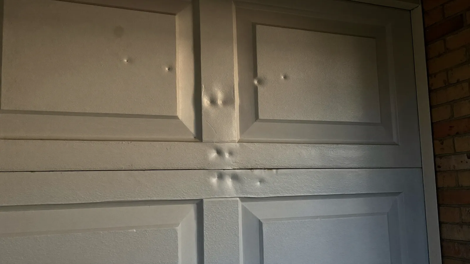 Close view of the upper panels of a white steel garage door on a West Texas brick home, round hail dents pressed into the raised panels and the rail between them